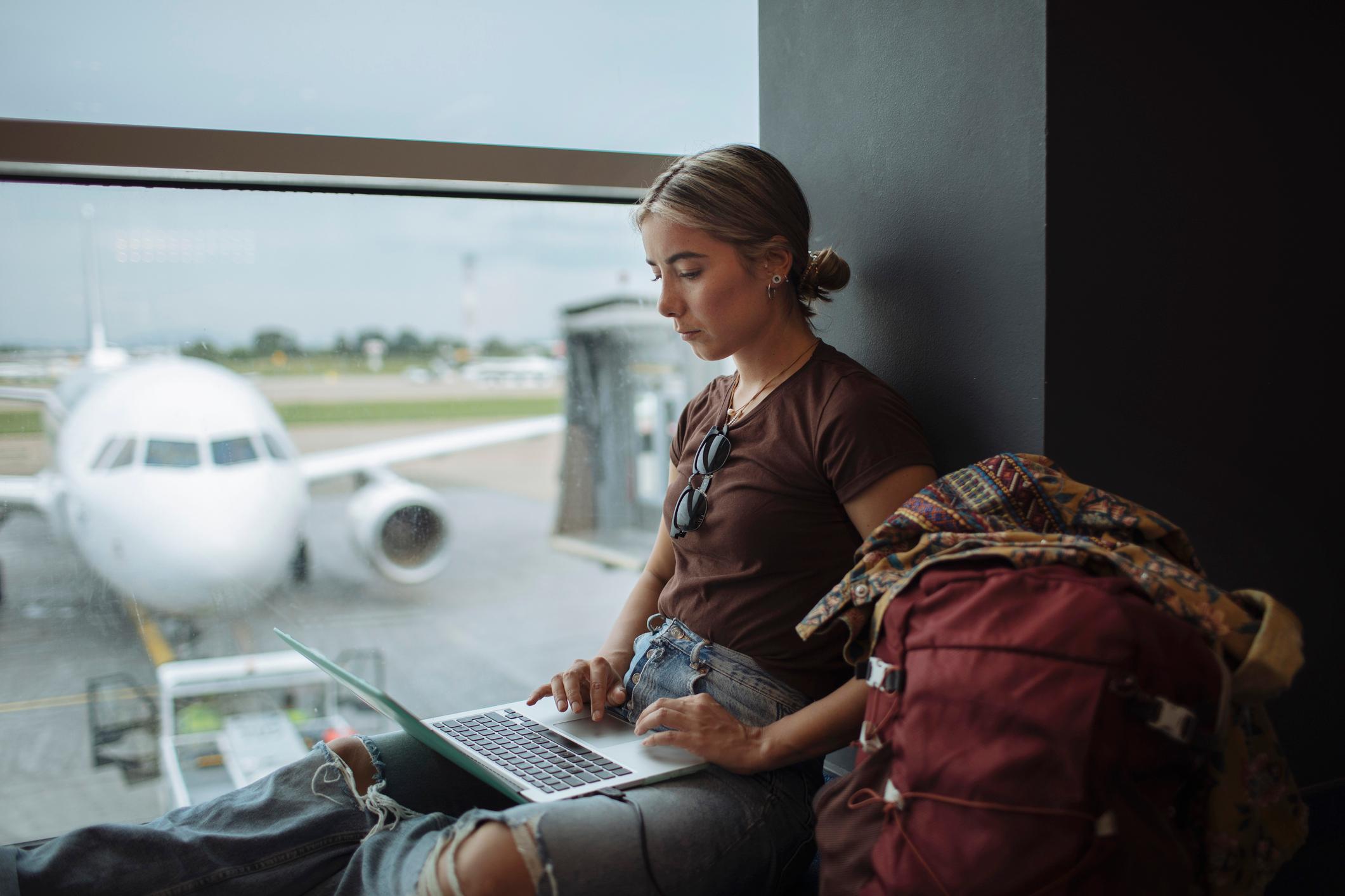 A young woman is not wasting time while waiting for her flight but is working on her laptop