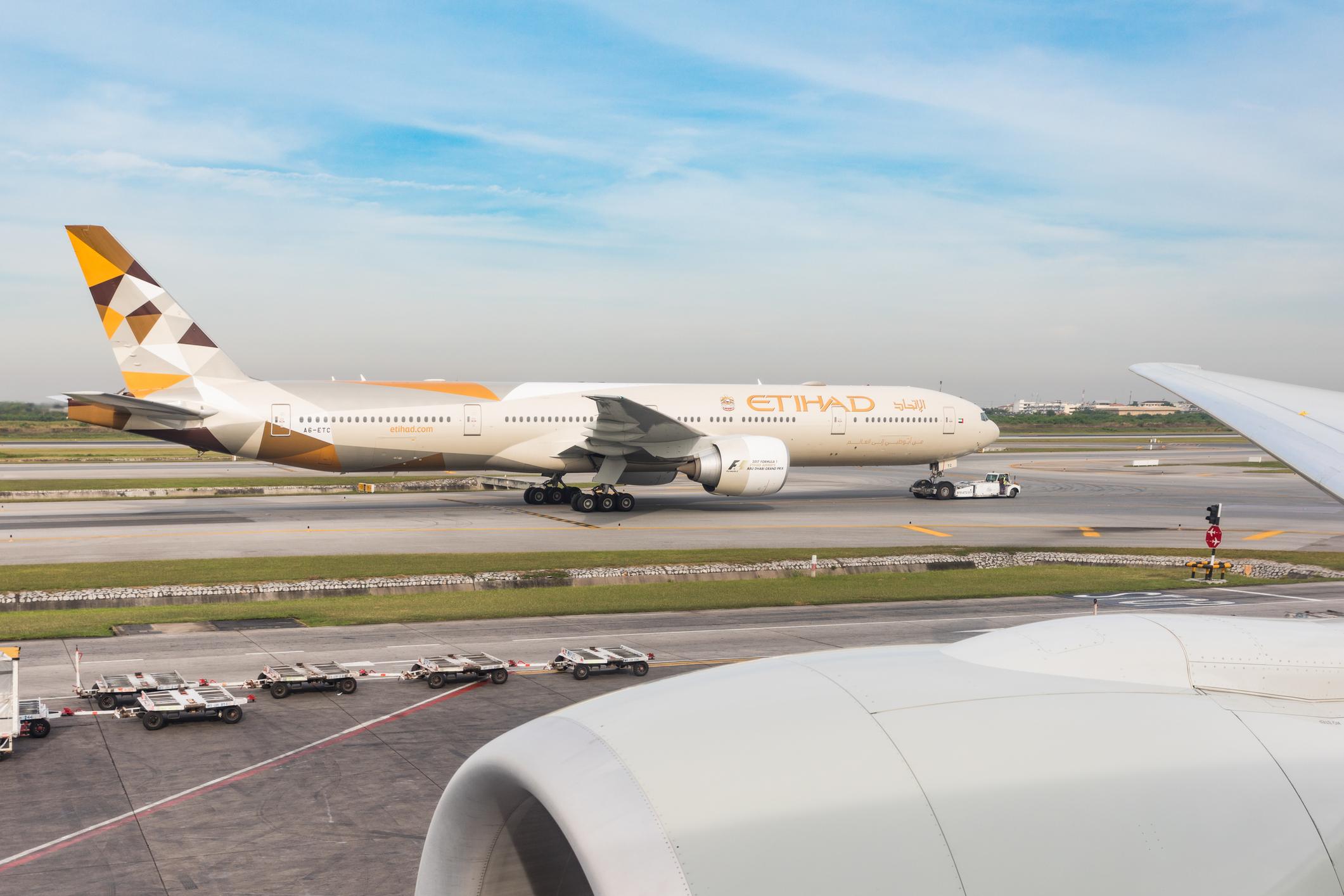 Bangkok: Etihad Boeing 777 on taxiway at Suvarnabhumi airport pulled by a tug to departing position. View from over wing seat on a Boeing 777, B777.
