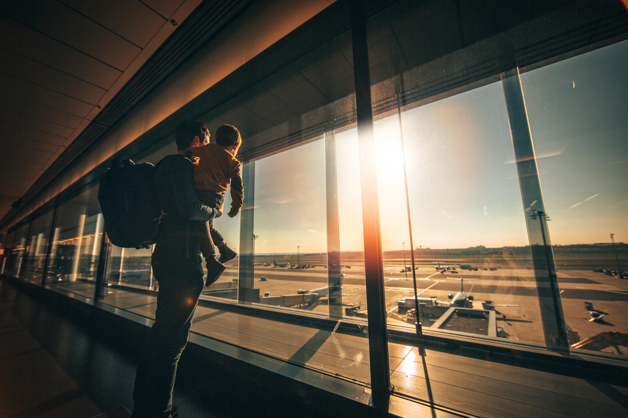 Young man and his son looking out of the window while waiting on airport lounge