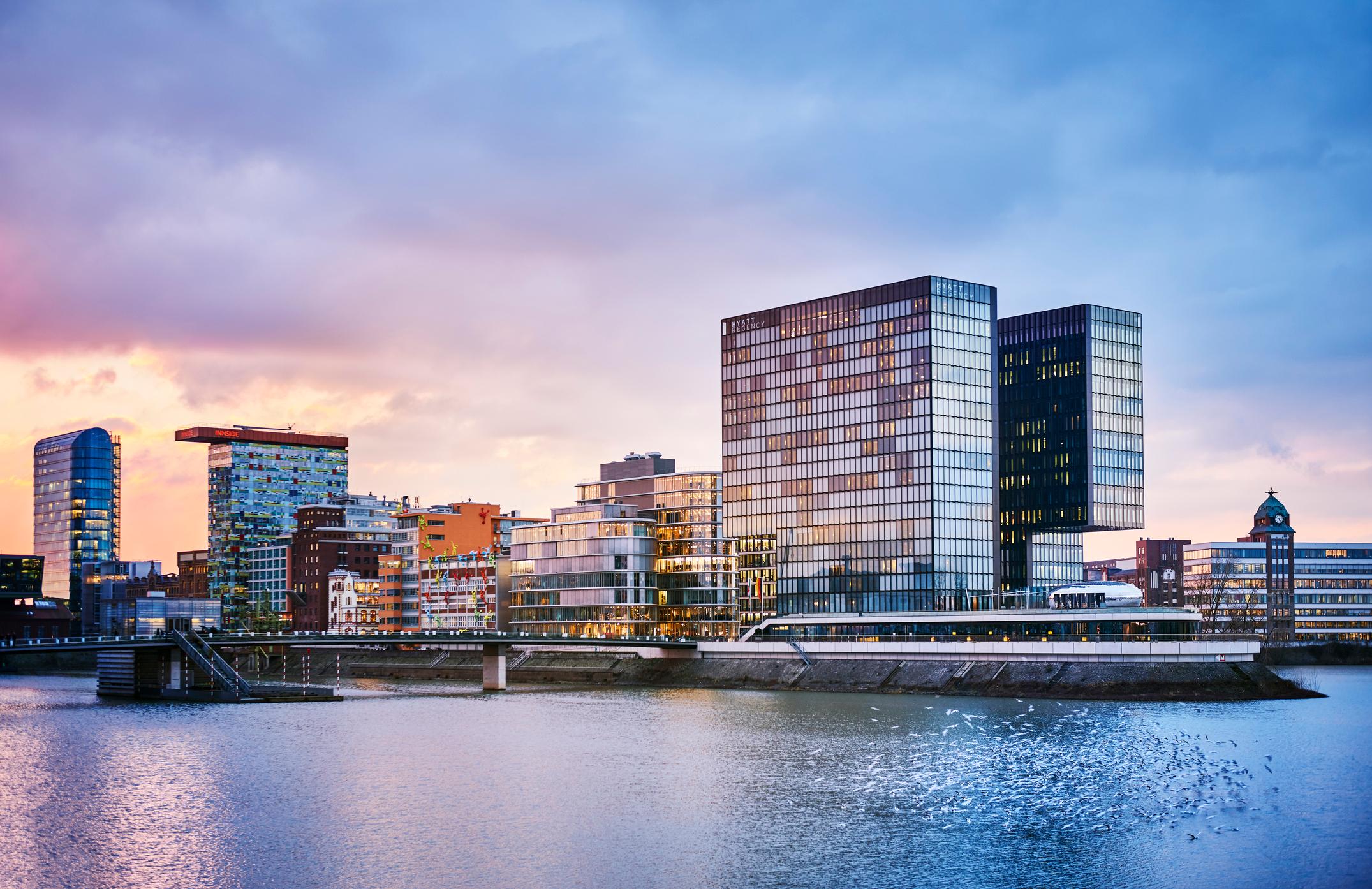 The Media Harbour at dusk, the Hyatt Regency Hotel on the right side and diverse Office Buildings on the left side. The river Rhine and birds in the foreground, long exposure.