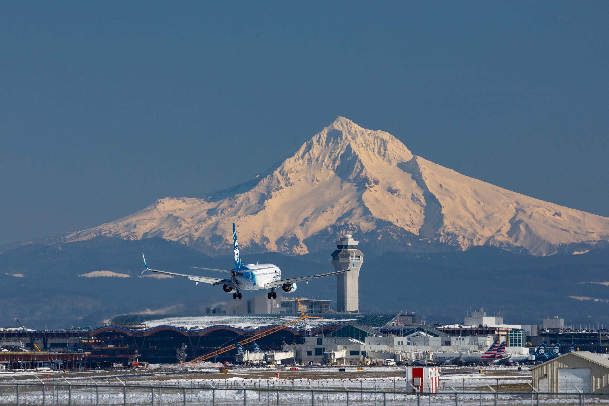 An Alaska Airlines 737 lands at a snow covered Portland International Airport with Mt Hood in the background.